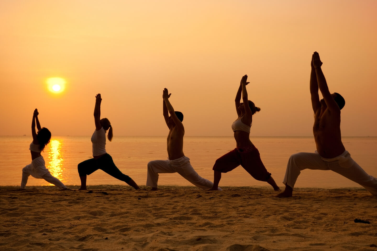 people doing yoga at sunset on the beach